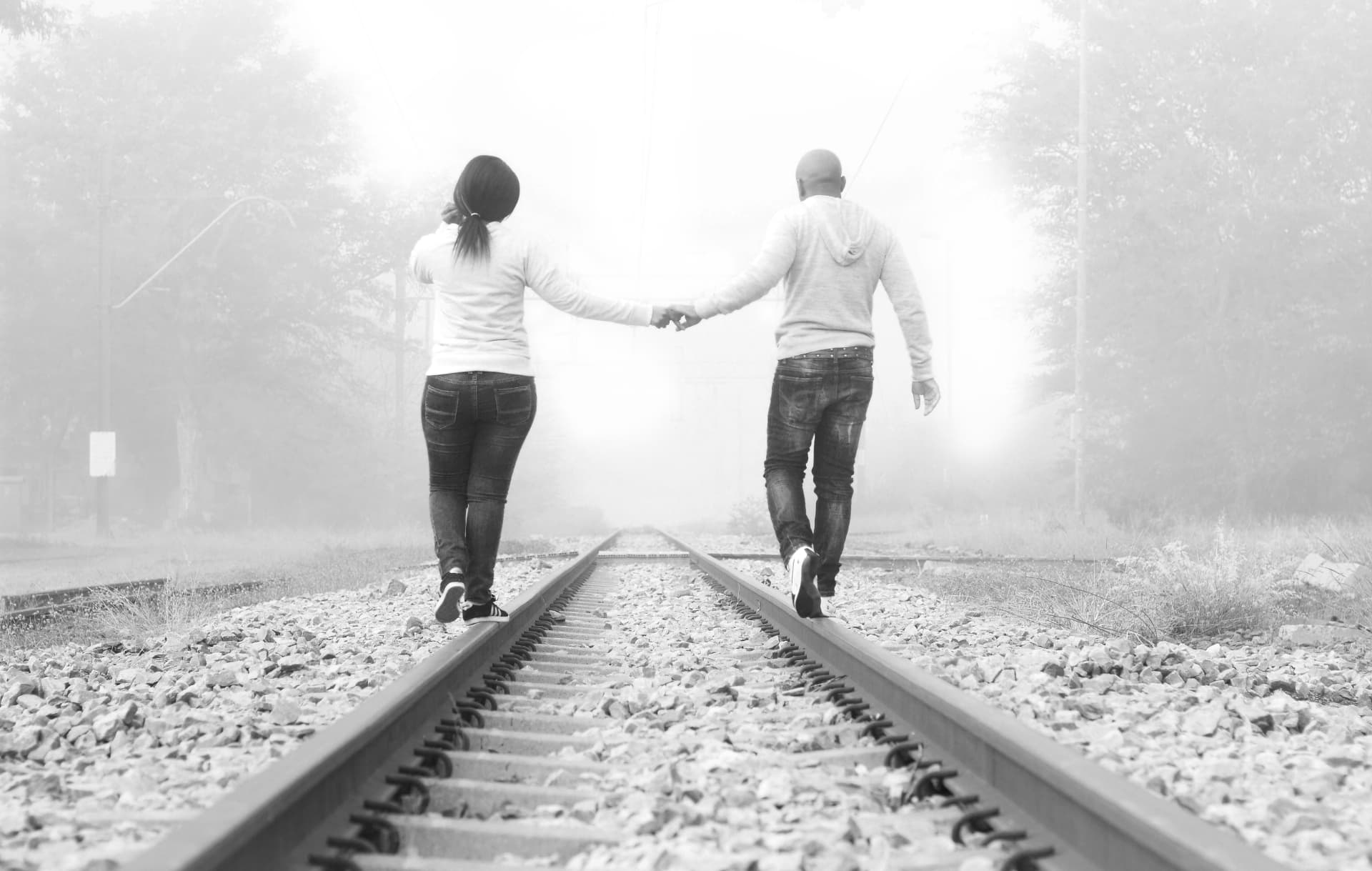 Black and white photograph of a couple walking railway tracks in mist