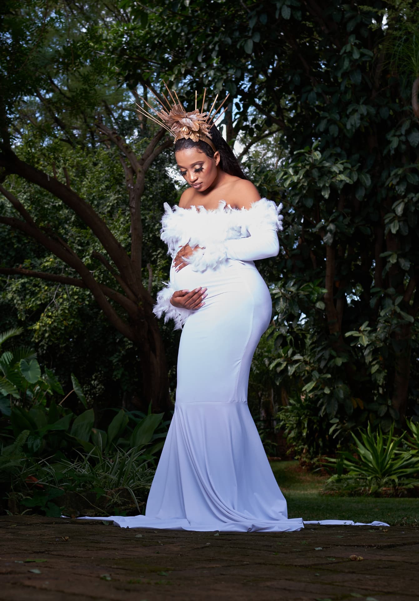 Outdoor maternity portrait in a white gown lit against dense greenery